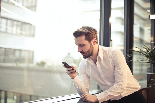 Homem apoiado na janela usando o telefone celular.