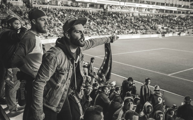 Homem branco na arquibancada de estádio de futebol com expressão brava.