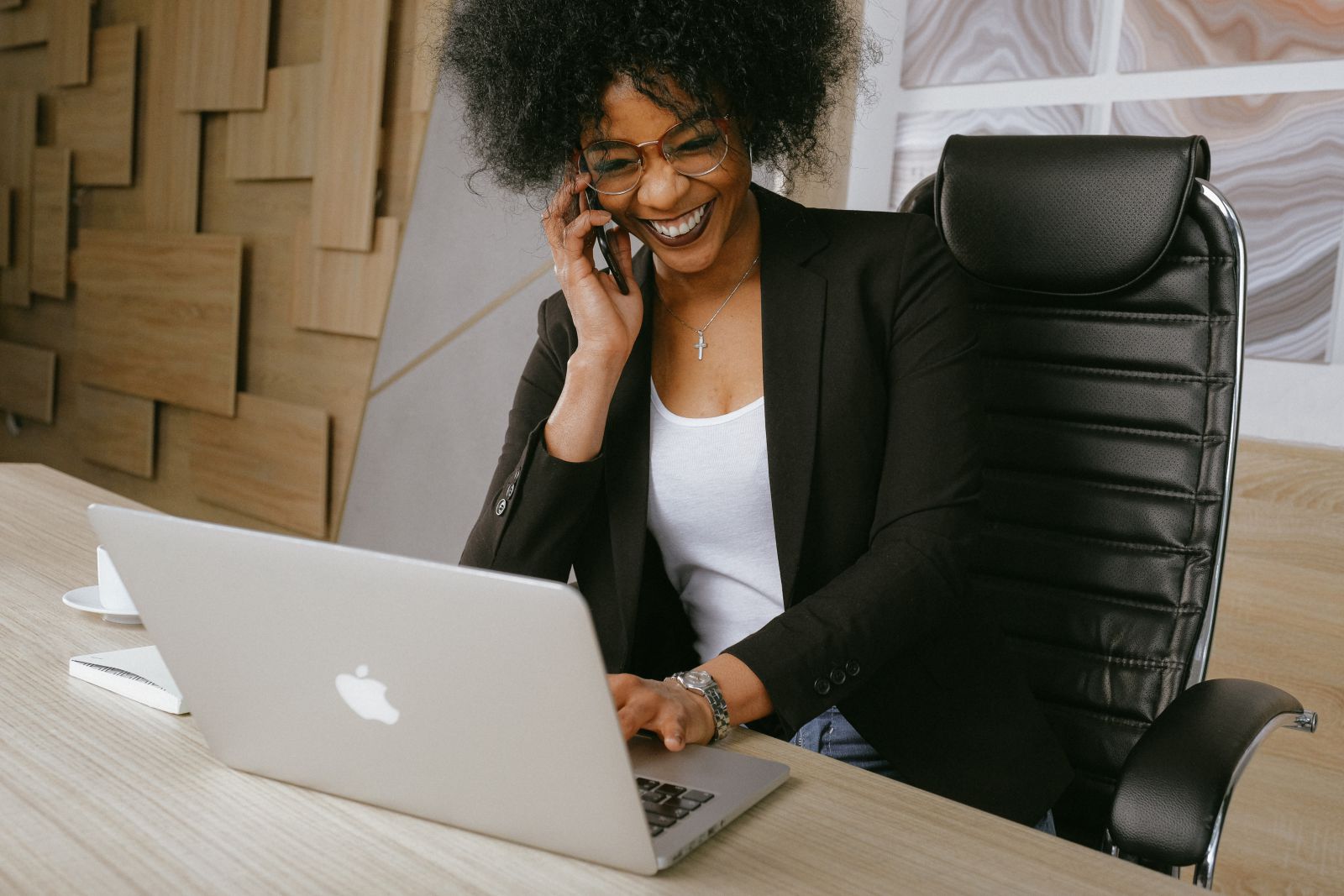 Mulher em seu escritório sorrindo ao falar com alguém no celular