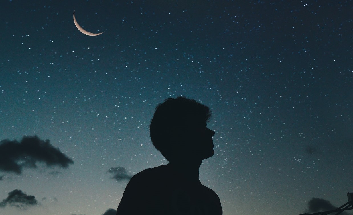 brenoanp  / Pexels Silhueta de um homem com o céu estrelado de fundo e a lua posicionada à esquerda