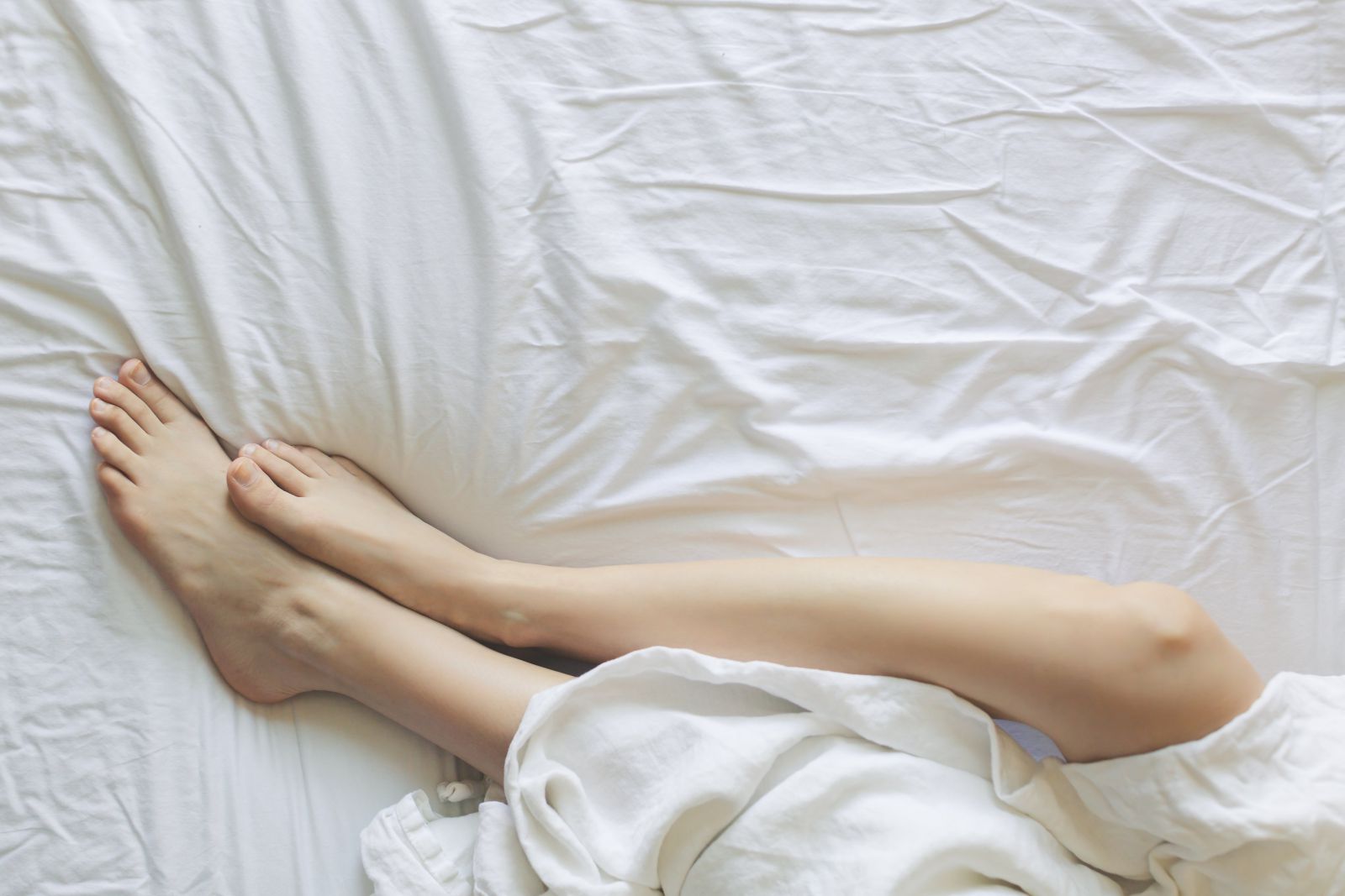 Mulher deitada na cama com os pés juntos