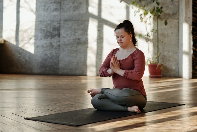 Mulher sentada no chão, de pernas cruzadas e olhos fechados, meditando