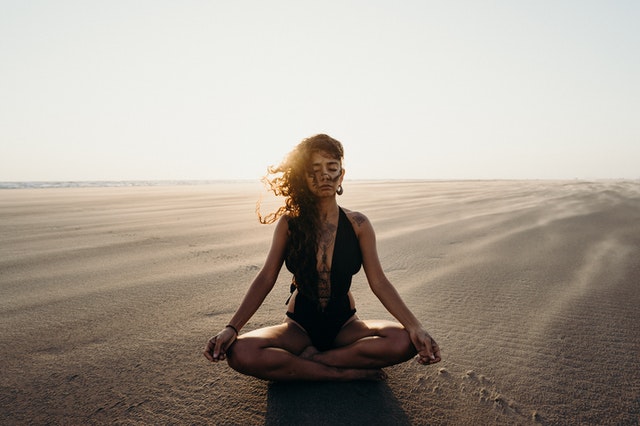 Mulher sentada na areia, de maiô, meditando