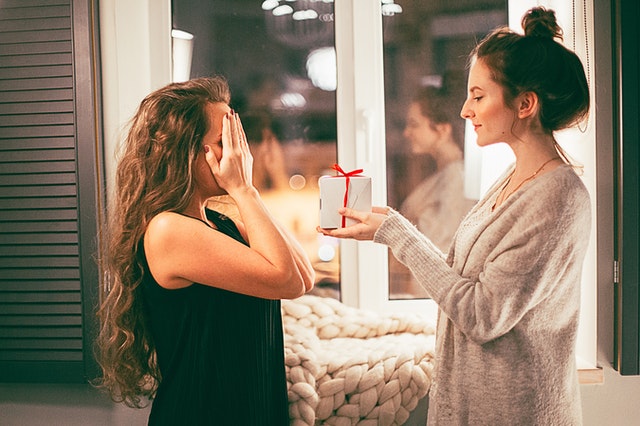 Mulher de olhos fechados recebendo um presente de Natal de uma outra mulher
