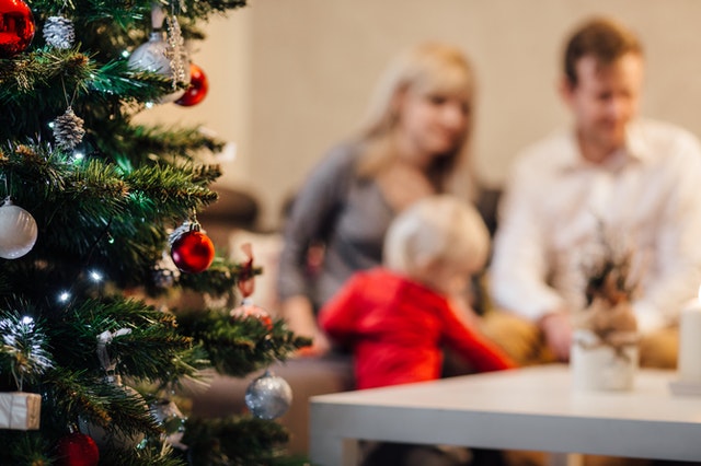 Árvore de natal com família brincando ao fundo.