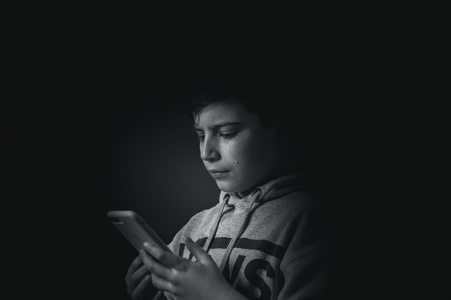 Menino branco chorando enquanto segura celular.