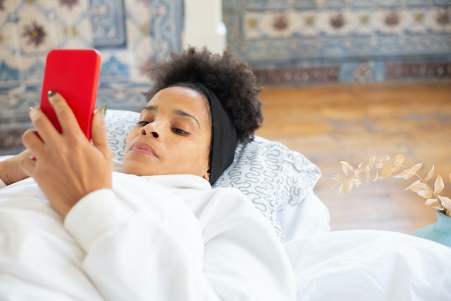 Mulher negra deitada usando celular.
