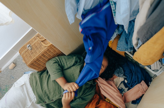 Mulher branca deitada no chão com roupas coloridas em cima.