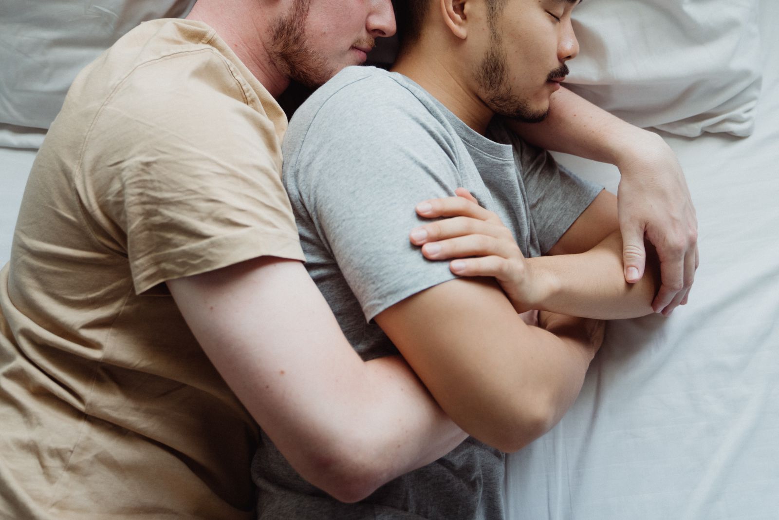 Casal de homens deitados na cama abraçados