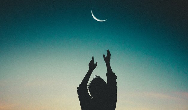 luizclas / Pexels Silhueta de uma pessoa com os braços levantados tentando alcançar a Lua Nova no céu