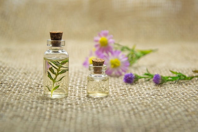 Pequenos potes de vidro com broto dentro e flores roxas atrás.