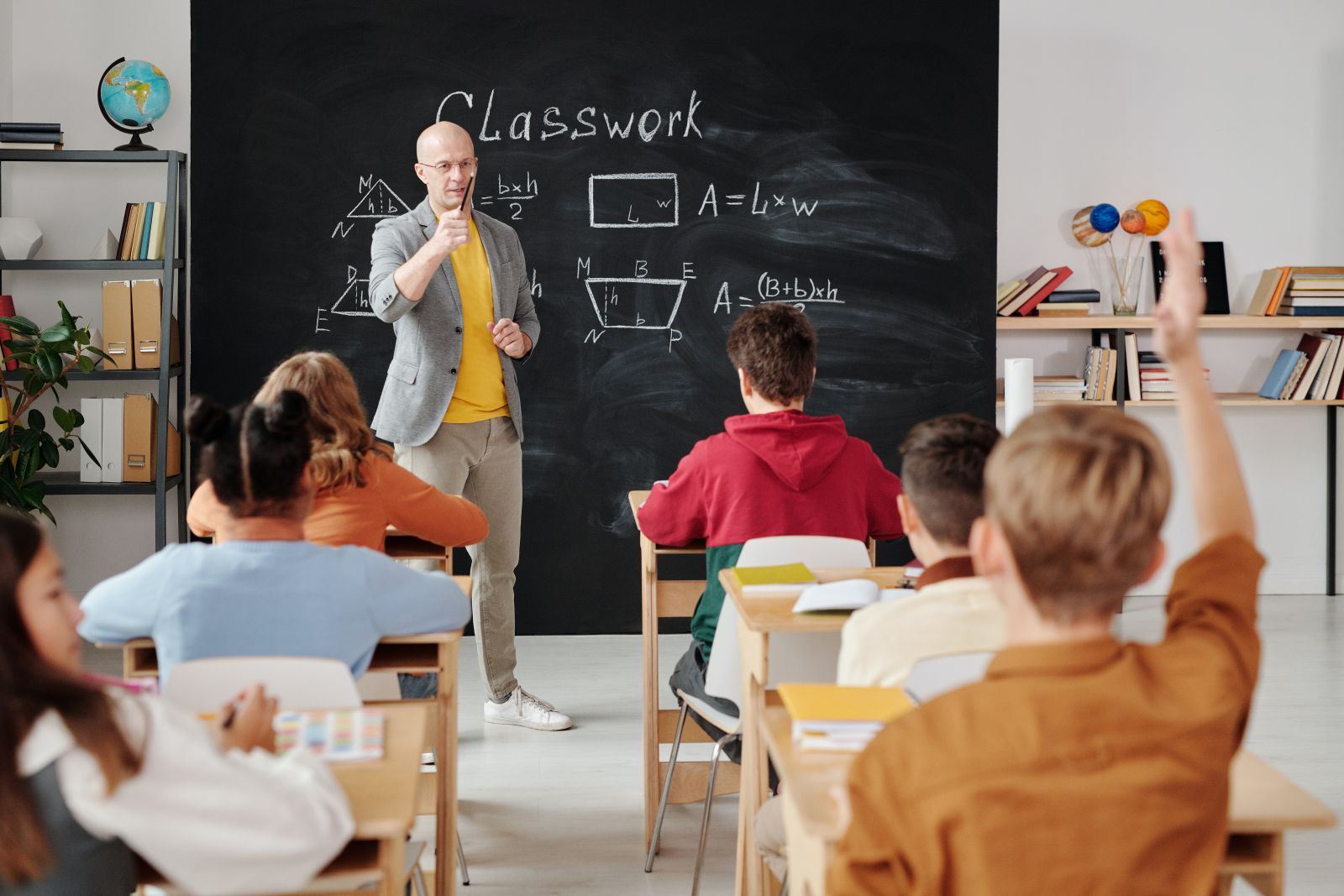 Sala de aula com alunos e professor ao lado da lousa 