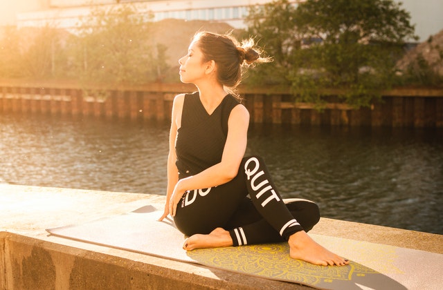 Mulher sentada ao lado de um rio, alongando-se e meditando