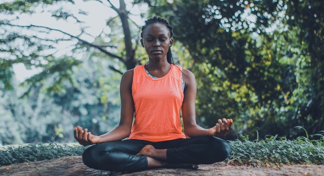 Mulher sentada meditando de olhos fechados em contato com a natureza