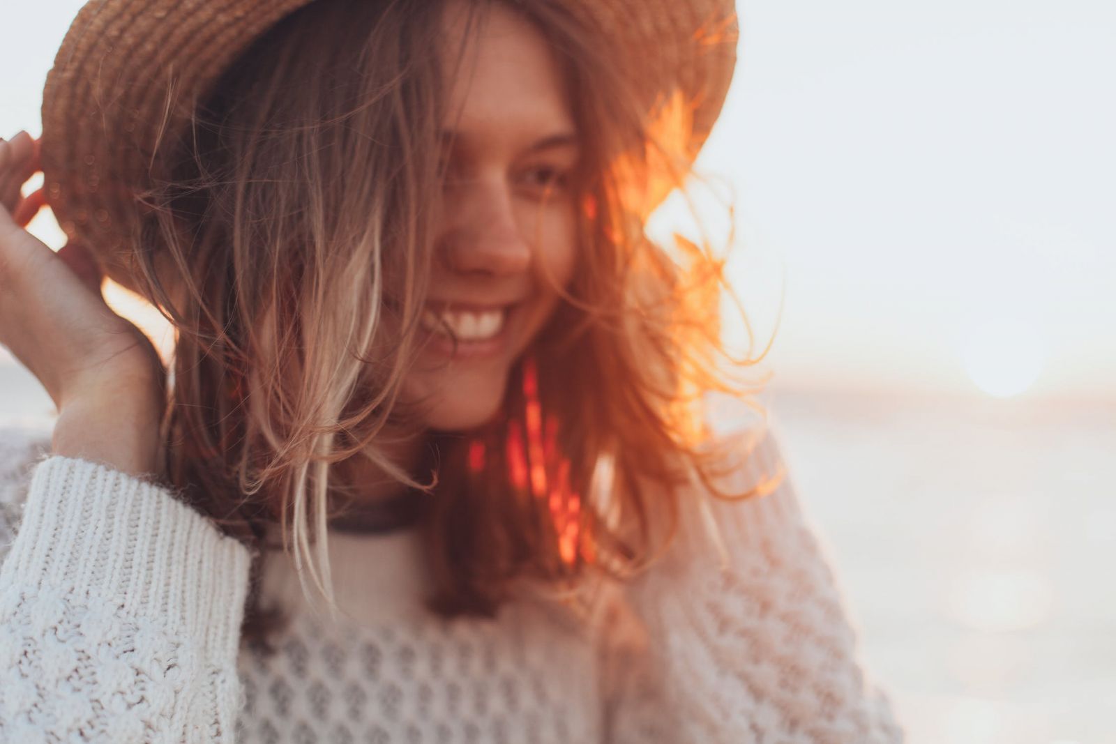 Mulher sorrindo segurando chapéu na cabeça