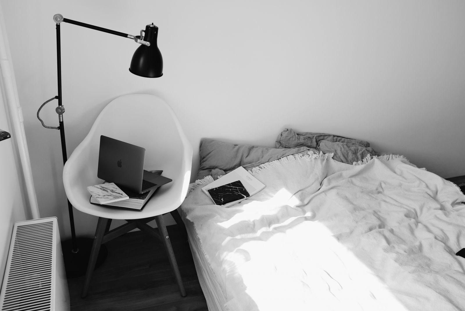 Cama ao lado de uma cadeira com um notebook aberto