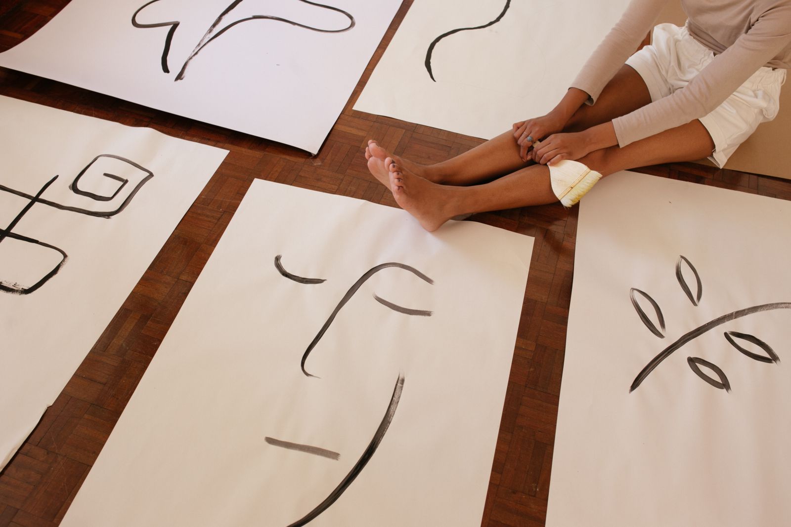 Mulher sentada segurando pincel ao lado de folhas com pinturas