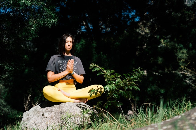 Mulher branca meditando sentada numa pedra.