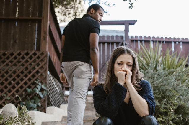 Mulher branca sentada triste e homem negro olhando para trás.