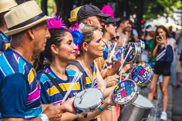 Pessoas brancas com roupas coloridas tocando pandeiro.