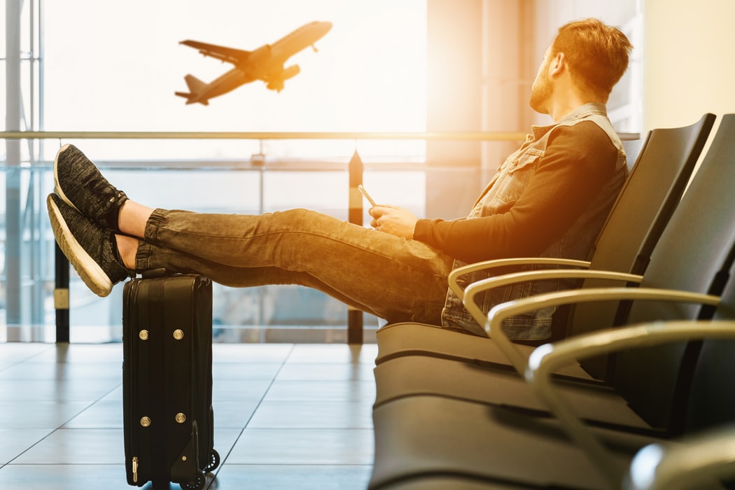 Homem branco sentado num banco do aeroporto.