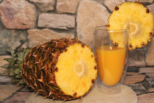 Copo com líquido amarelo e abacaxi ao lado.