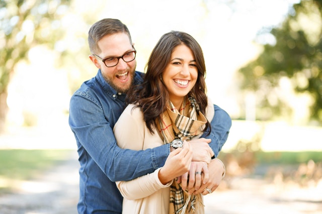 Casal abraçado com homem atrás e ambos sorrindo