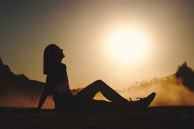 Silhueta de mulher sentada de lado num pôr-do-sol.