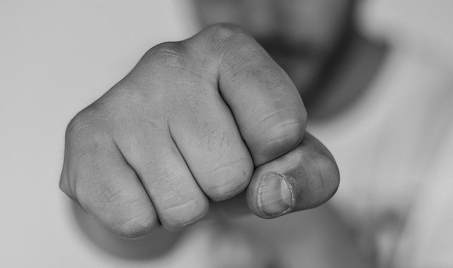 Mão fechada em foco com rosto de homem ao fundo 