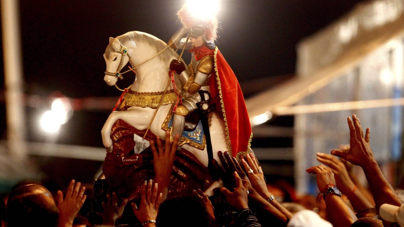 Multidão de pessoas levantando uma estatueta da imagem de São Jorge, à noite.