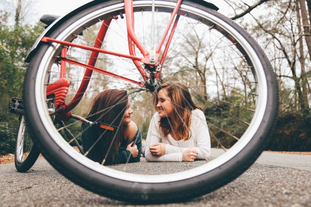 Mulheres brancas deitadas no asfalto atrás de bicicleta.