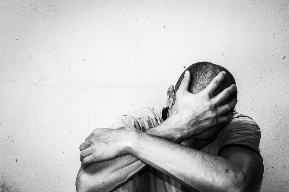 Homem branco de cabeça baixa e mão na cabeça.
