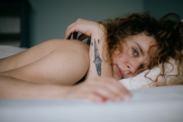 Mulher branca deitada de bruços numa cama branca.