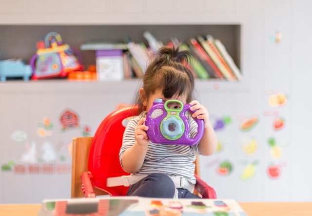Bebê branca segurando câmera fotográfica de brinquedo.