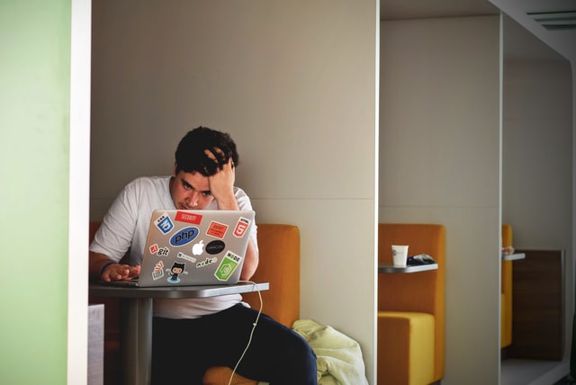 Homem branco sentado com a mão no cabelo enquanto usa um notebook.