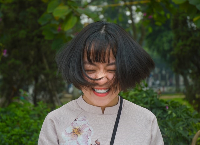 Mulher asiática com expressão sorridente e cabelos balançando.