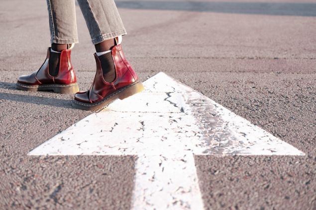 Pés calcando botas e caminhando na direção contrária da seta desenhada no chão.