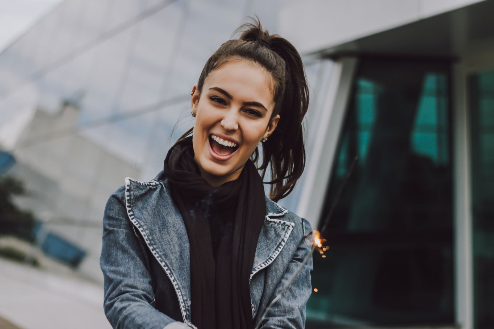 Mulher sorrindo em frente a um prédio segurando uma vela acesa