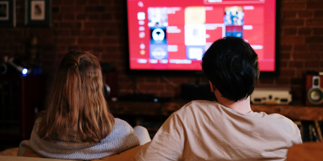 Homem e mulher sentados em sofá assistem à televisão.