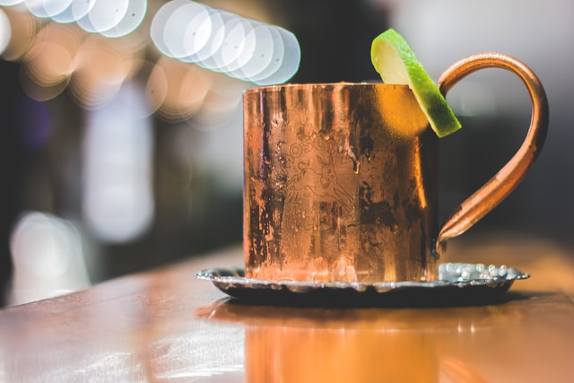 Caneca bronze com gotas de água ao redor e rodela de limão na borda.