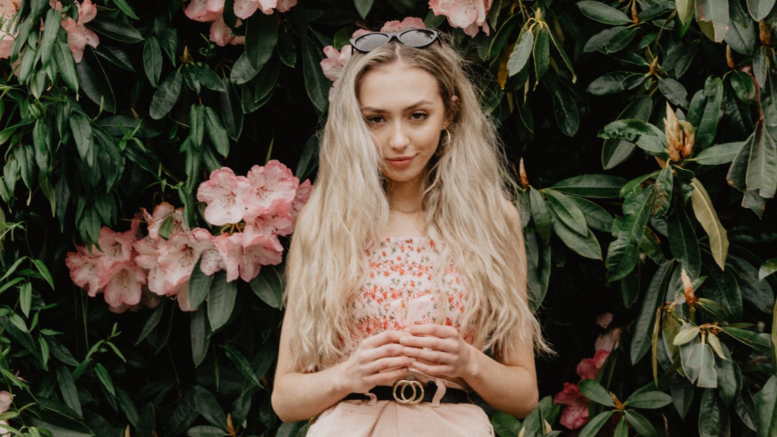 Retrato de uma mulher na frente de um muro de flores.