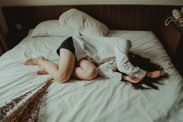 Mulher branca deitada numa cama.